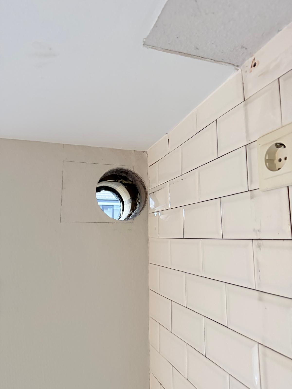 Afzuigkap gat in witte betegelde keukenmuur hoog bij plafond