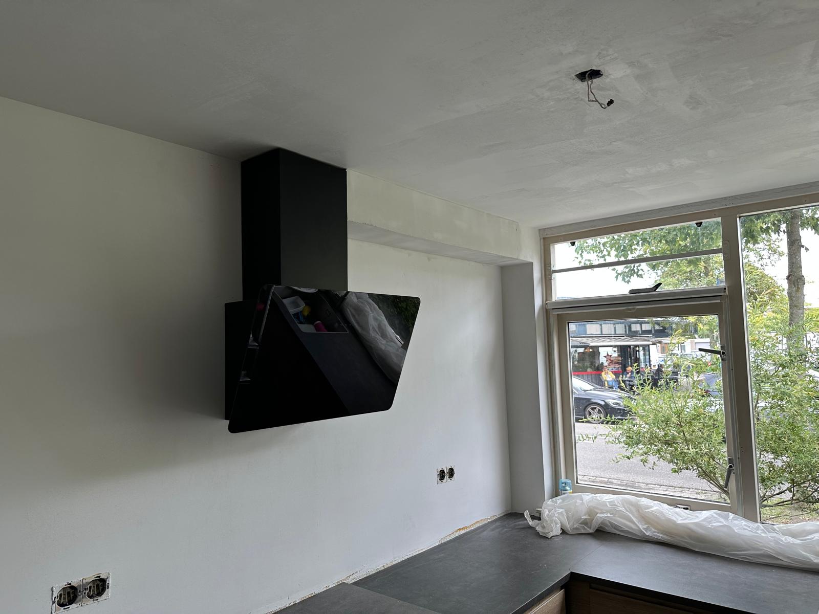 Zwarte schuine afzuigkap tegen nieuw gestuct beton