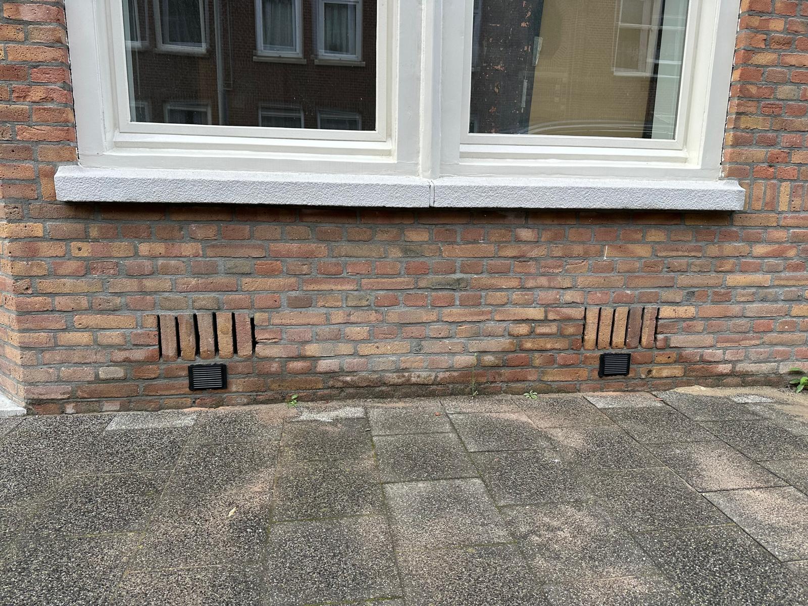 Twee ventilatiepunten geboord in baksteengevel met zwarte roosters