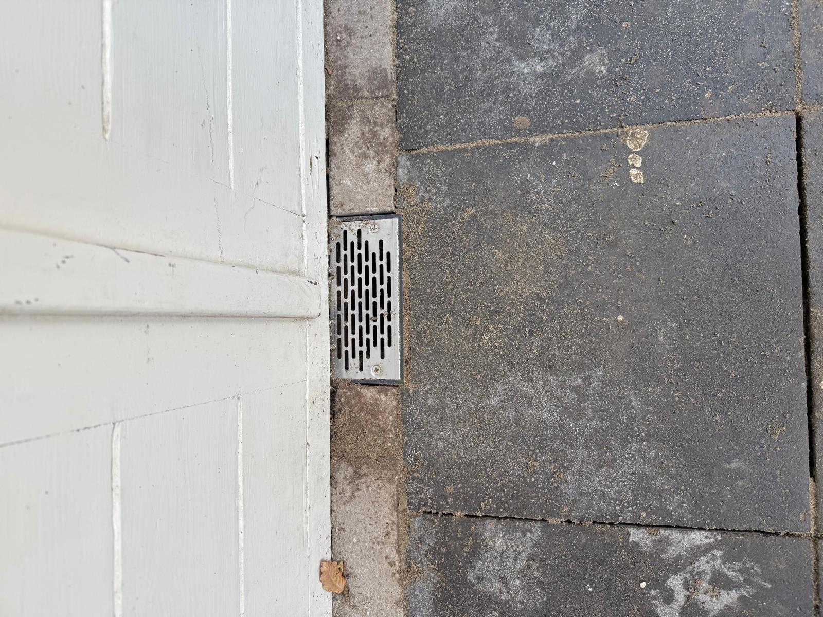 RVS ventilatierooster ingebouwd in vloerdrempel naast witte deur