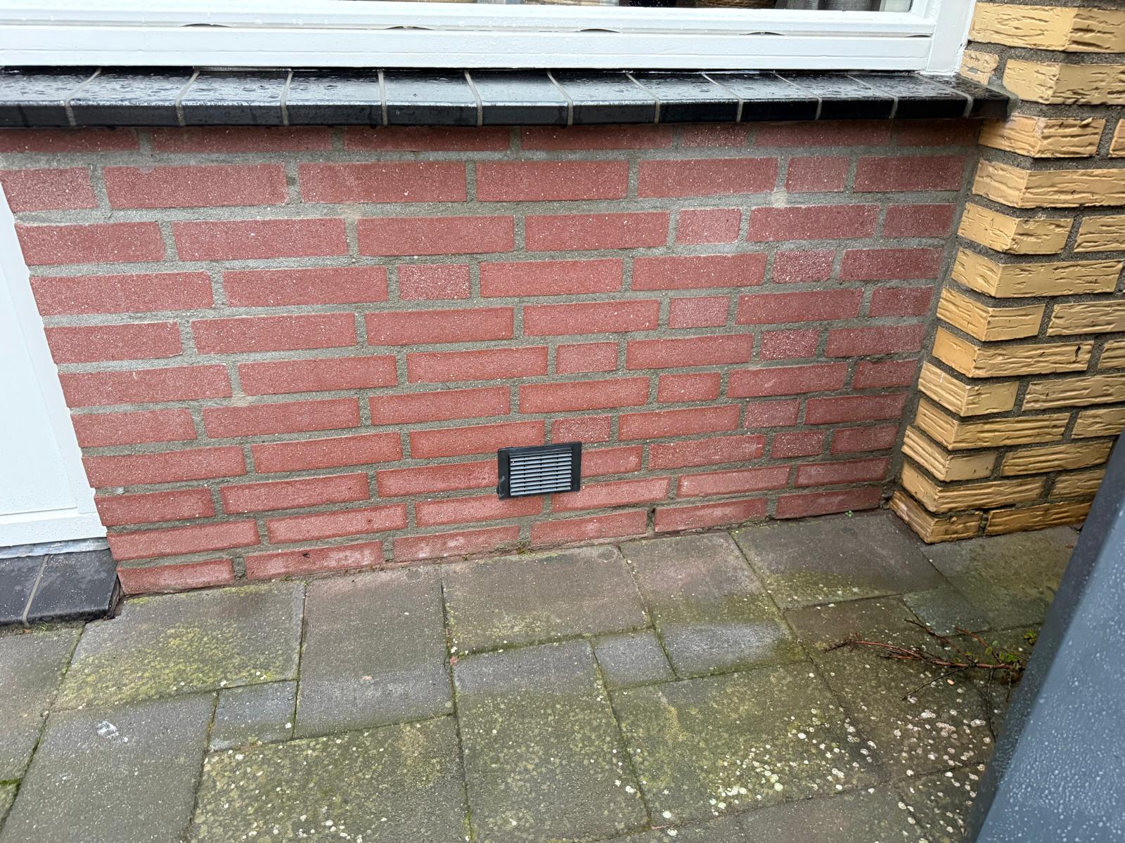 Zwart ventilatierooster in rode baksteengevel — nette afwerking