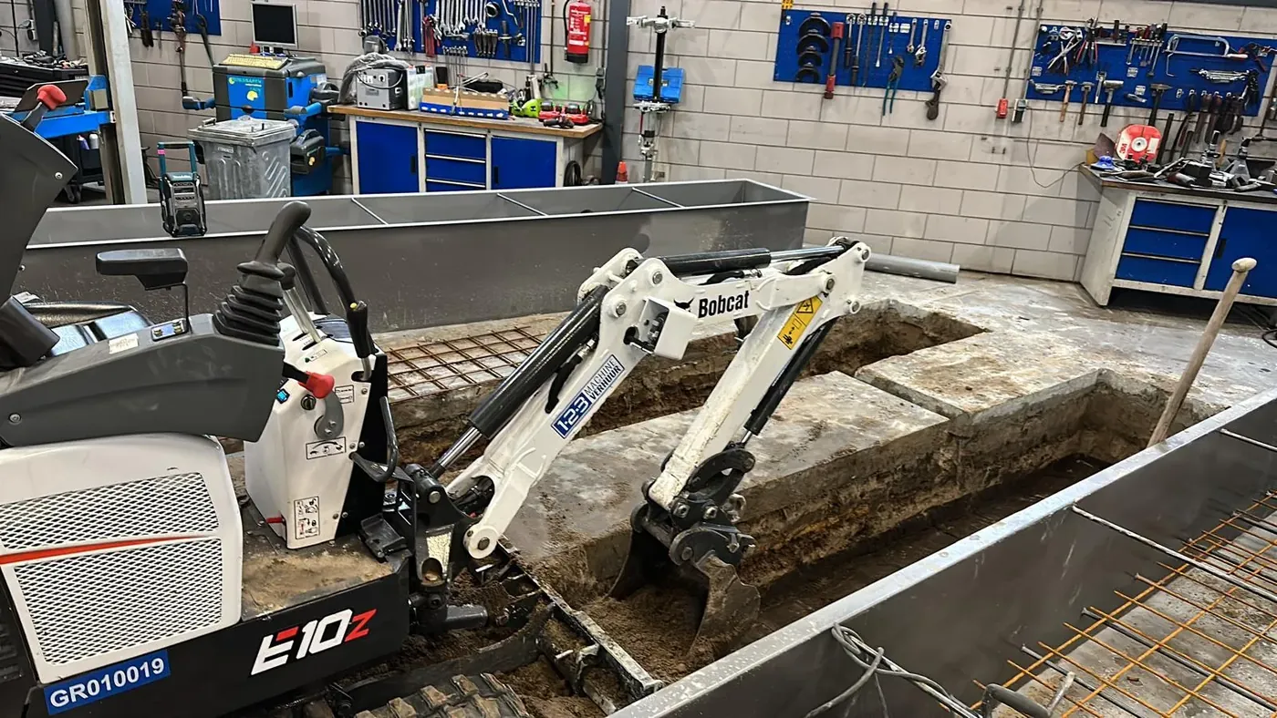 Bobcat E10z minigraver breekt betonvloer in werkplaats met zichtbaar wapeningsstaal