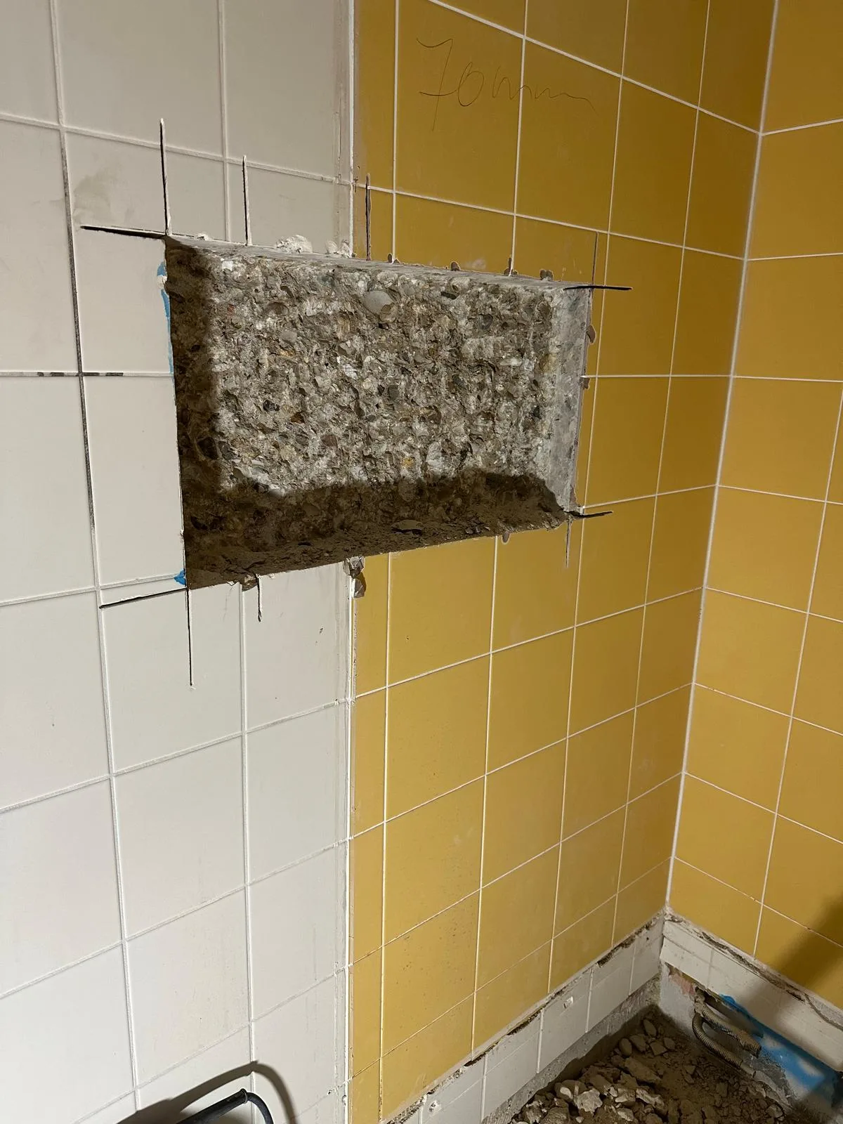 Opening gezaagd in betegelde muur badkamer — precisiewerk in gele en witte tegels
